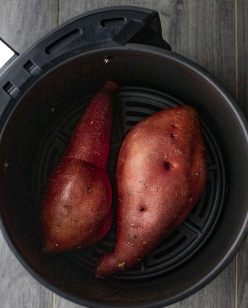 Two sweet potatoes in an air fryer basket.