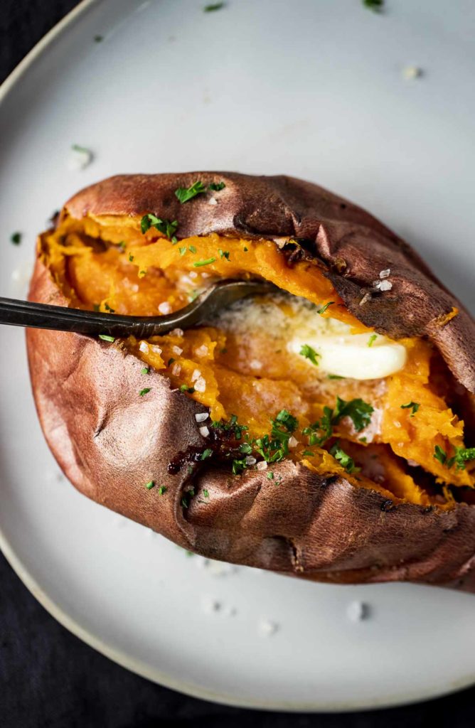Air fried sweet potato on a plate, topped with butter with a fork inserted into it.