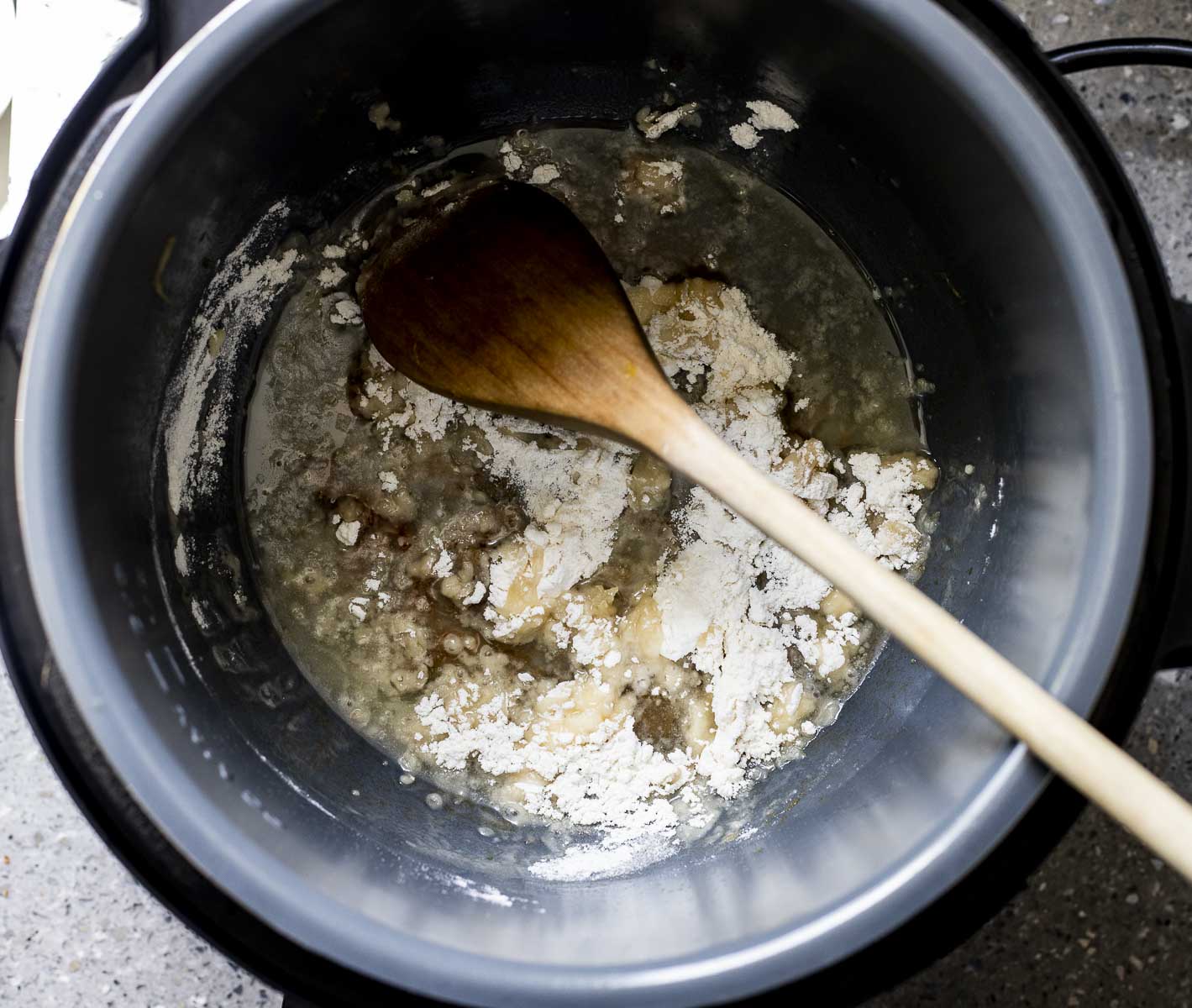 Oil and flour added to the Instant Pot with a wooden spoon stirring it.