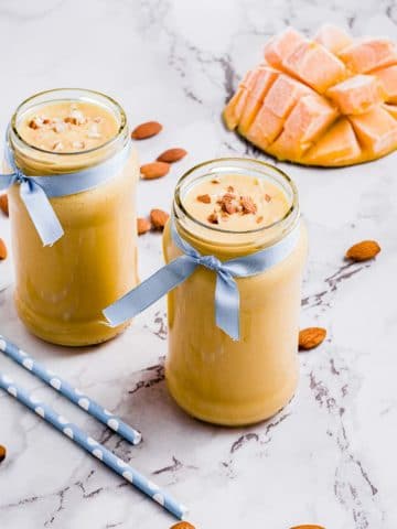 Two glasses of mango lassi with a ribbon around the rim.