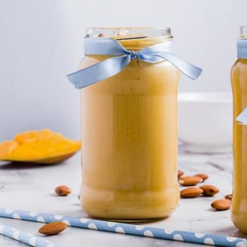 Jar of mango lassi with almonds and straws scattered around.