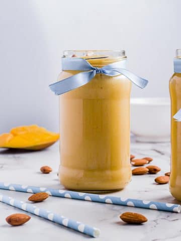 Jar of mango lassi with almonds and straws scattered around.