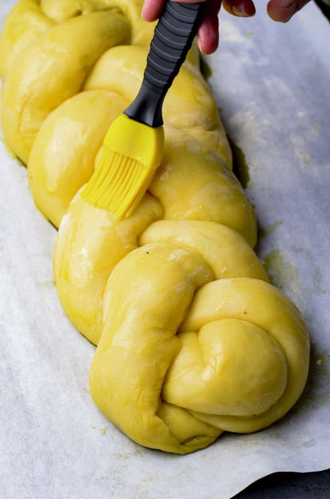 Brushing egg wash overtop of a braided challah.