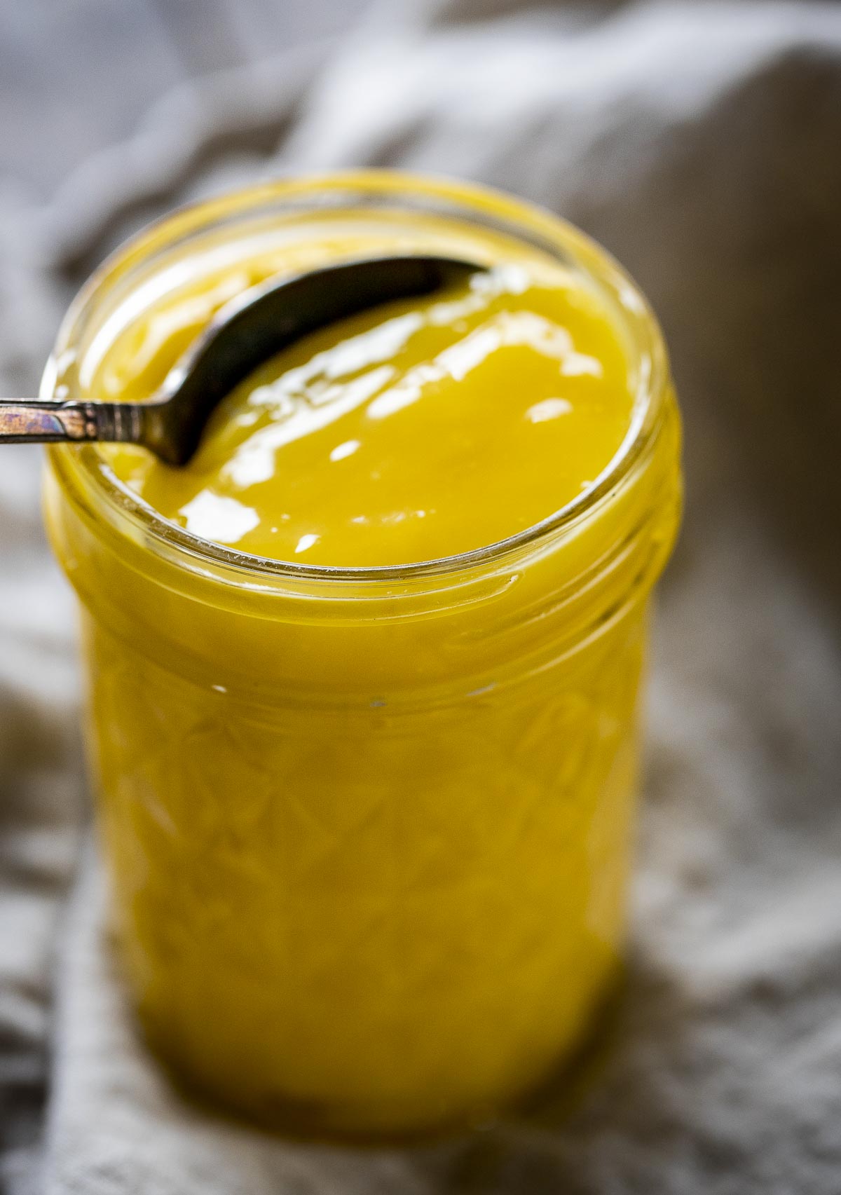 A mason jar of lemon curd with a spoon inserted.