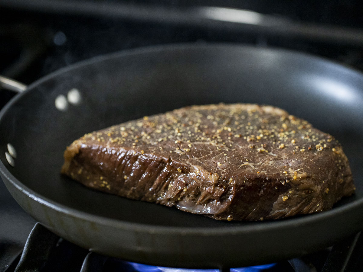 London broil being seared in a frying pan.