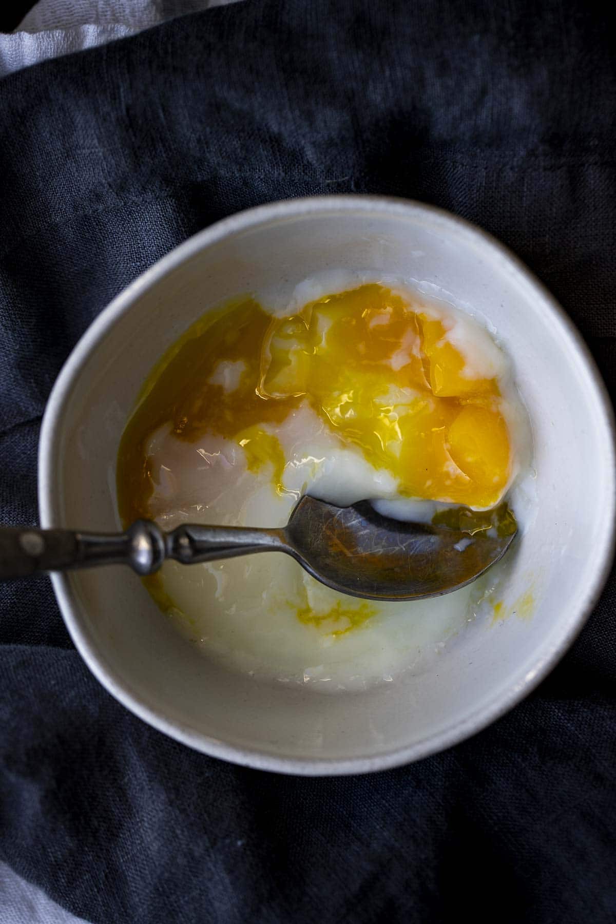 Overhead view of a poached egg in a bowl being eaten.