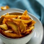 Dehydrated peach slices in a white bowl on a white plate.