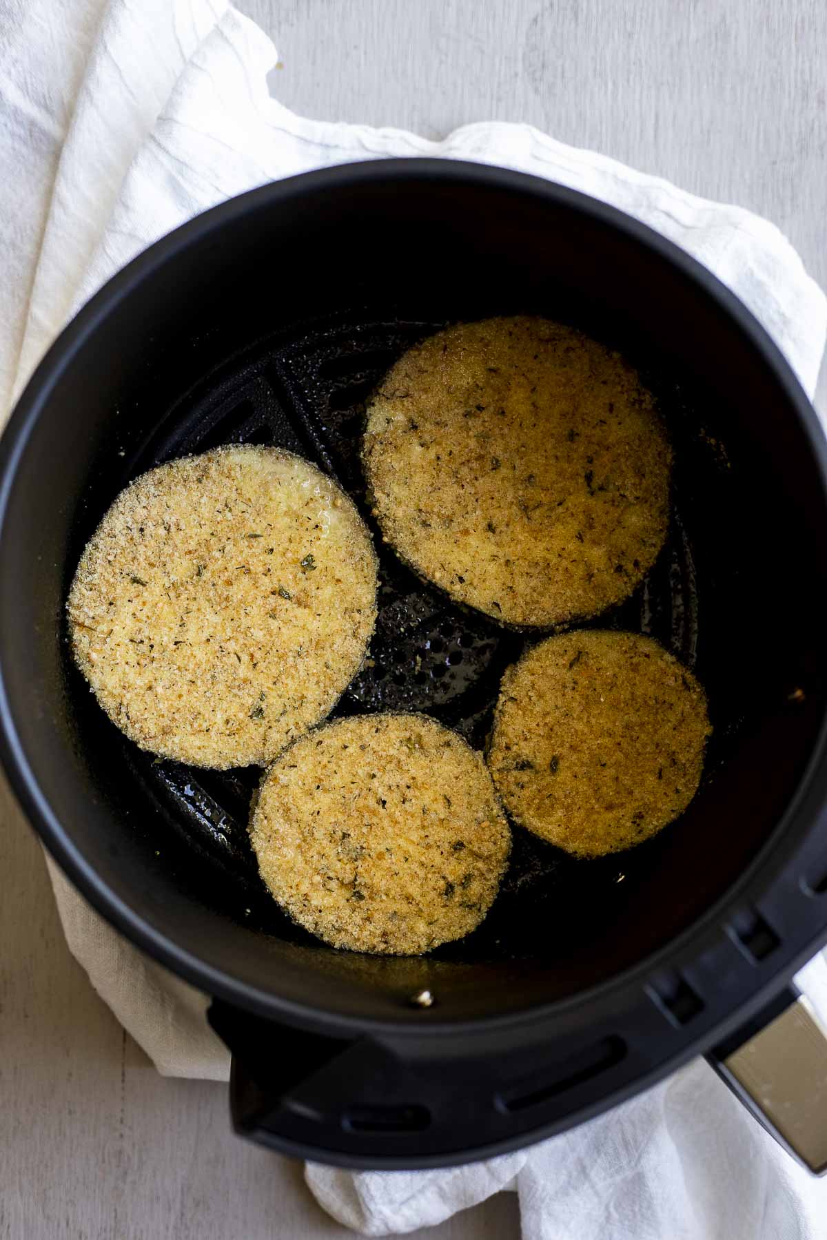 Four slices of breaded eggplant in an air fryer basket.