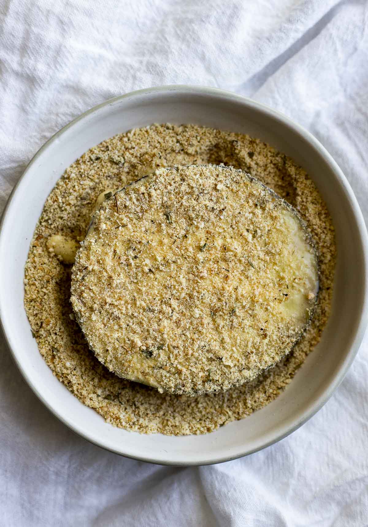 Slice of eggplant being coated in the breadcrumb mixture.
