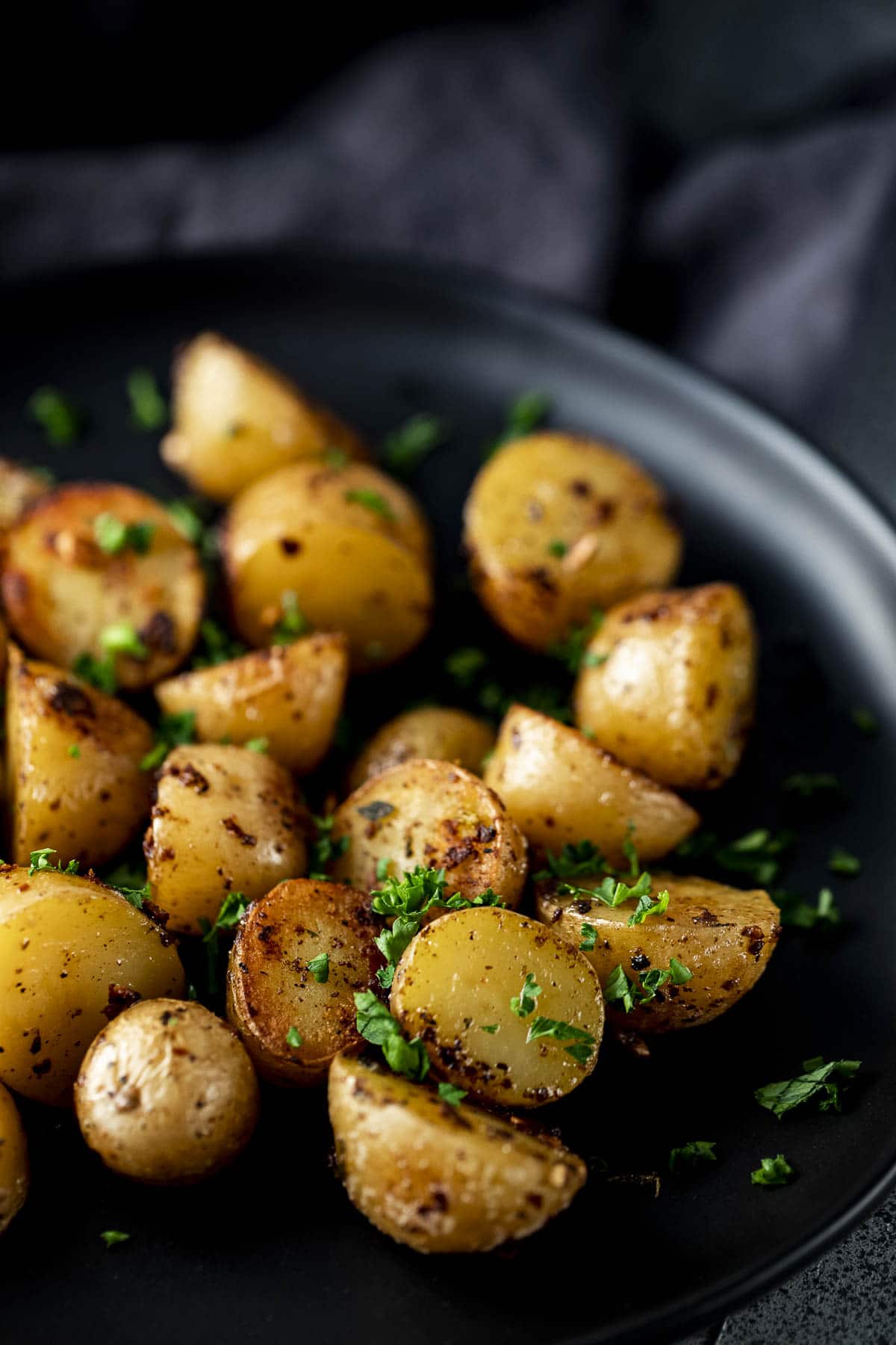 Cooked golden mini potatoes on a black plate.