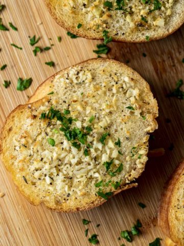 Close up view of a piece of garlic bread topped with chopped herbs.