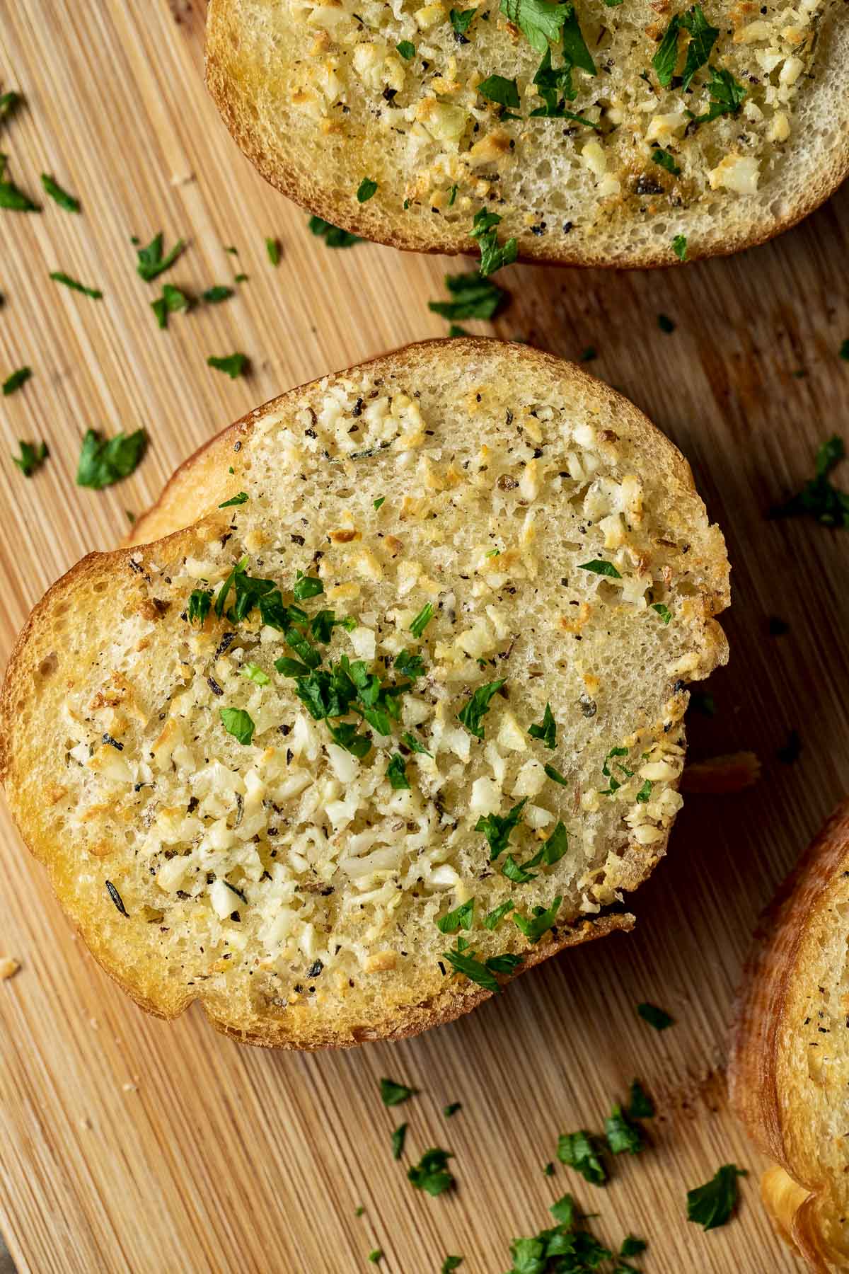 Close up view of a piece of garlic bread topped with chopped herbs.