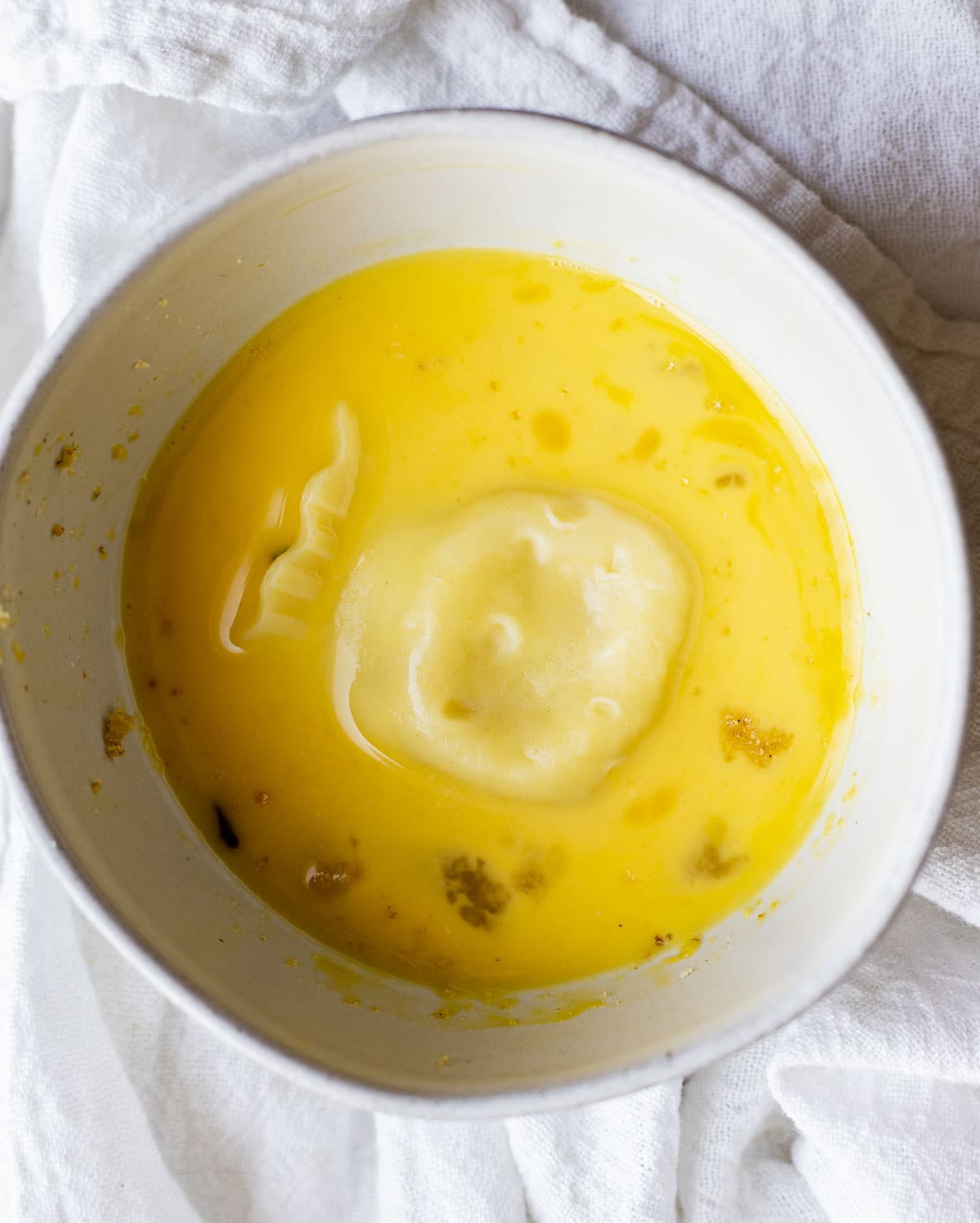 Ravioli being dipped in egg mixture in a white bowl.