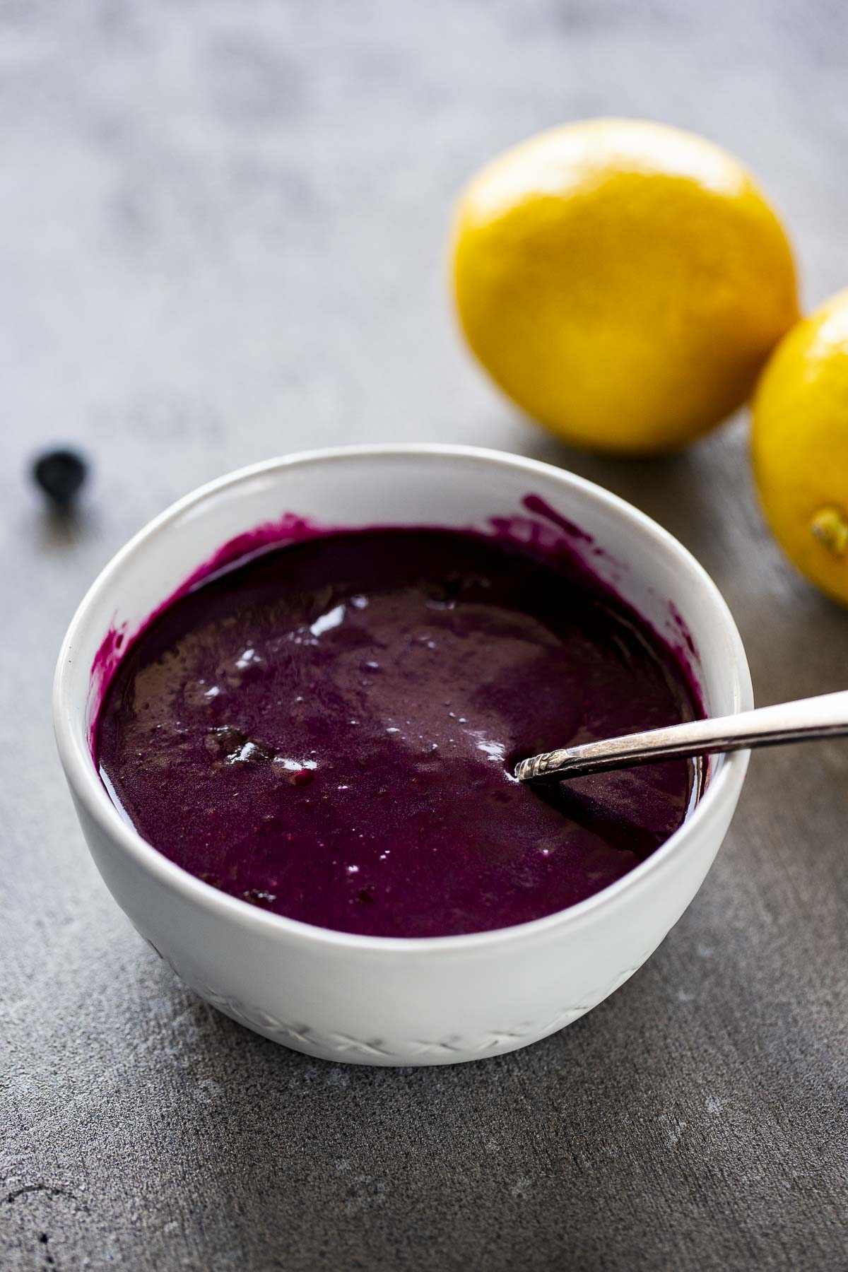 Blueberry curd in a white bowl with lemons in background.