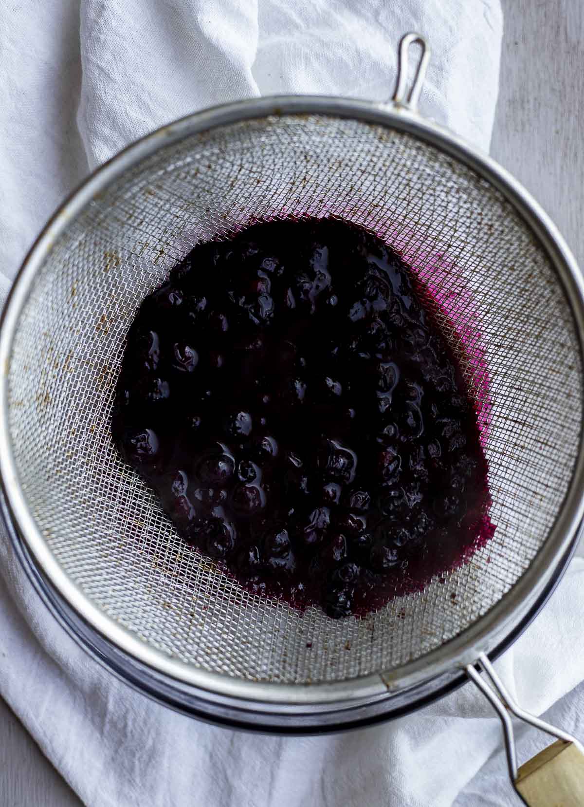 Blueberry mixture being strained in a mesh strainer.