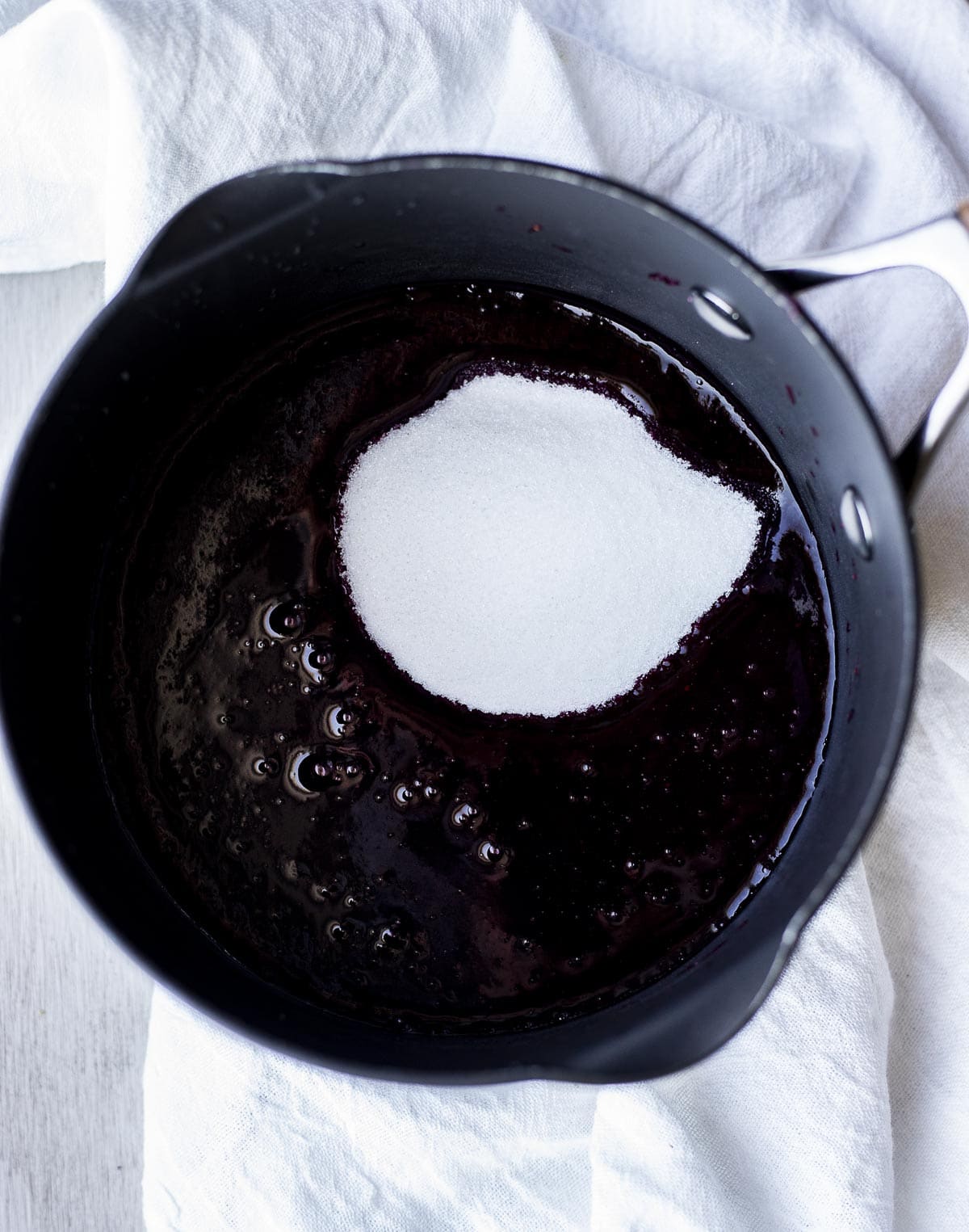 Sugar added to the blueberry mixture in a sauce pan.