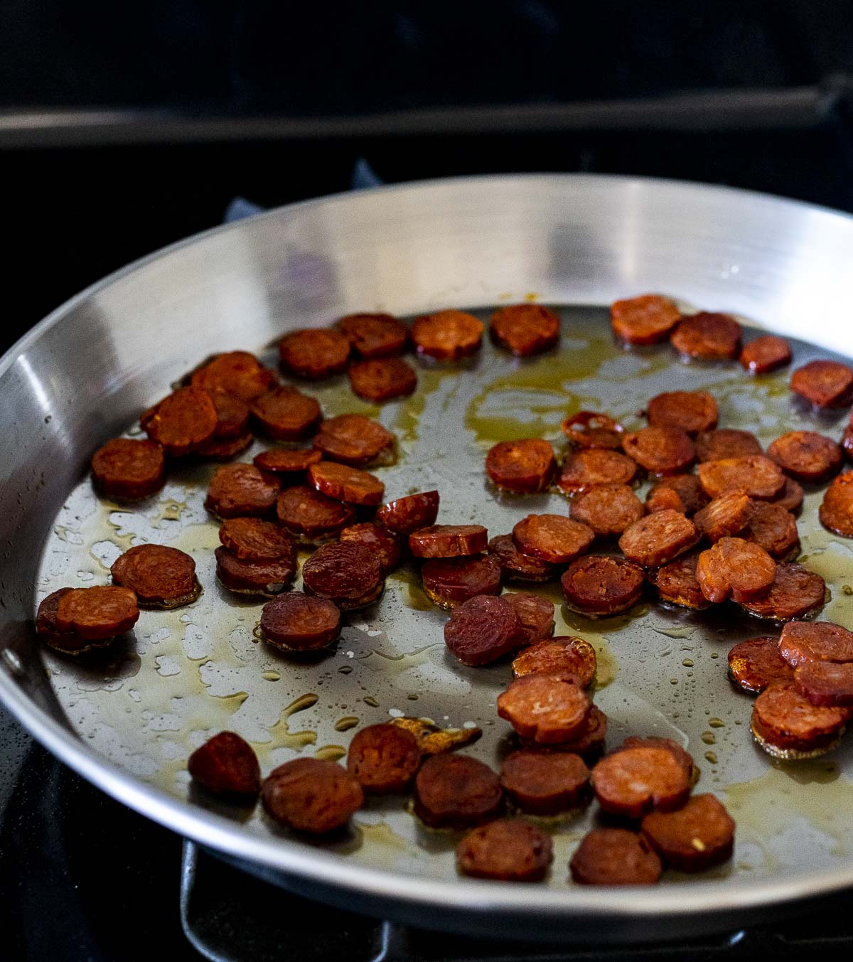Chorizo being browned in a paella pan.