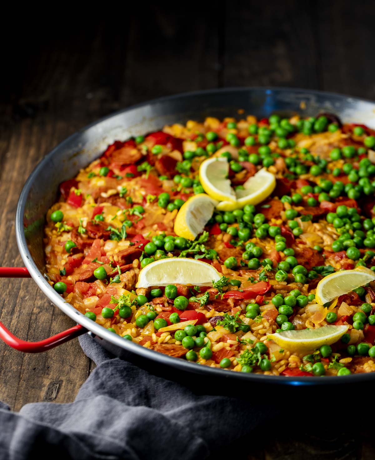 Side view of paella topped with green peas and lemon slices.