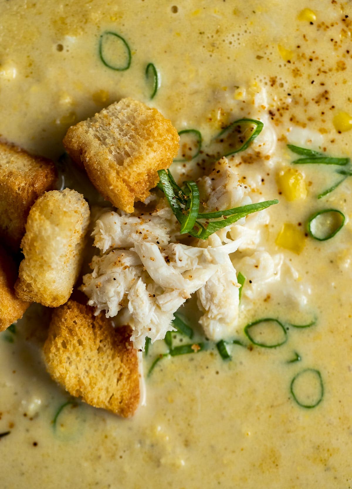 Close up of crab and corn bisque topped with green onion and croutons.
