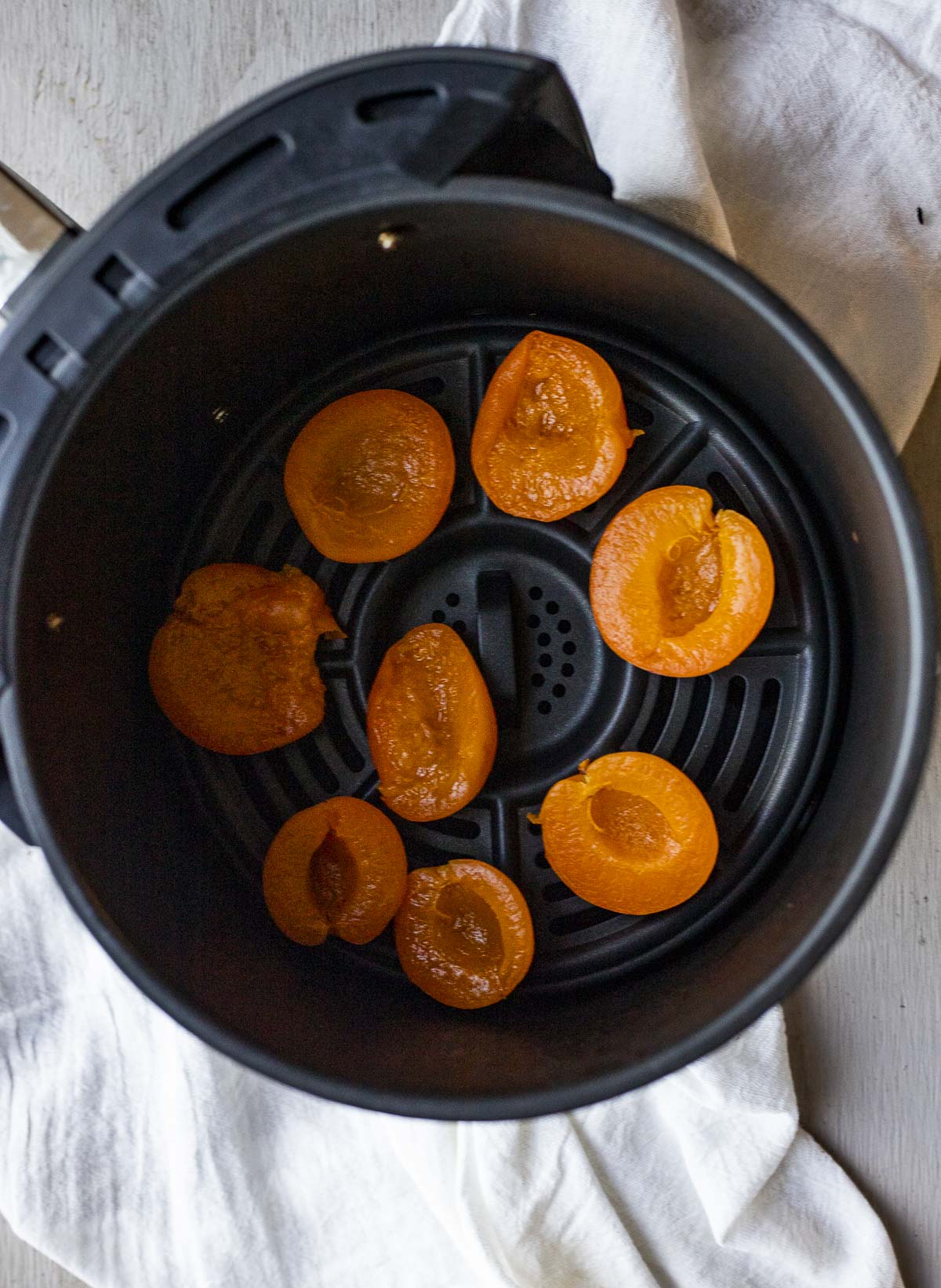 Apricot halves arranged in a single layer in an air fryer basket.