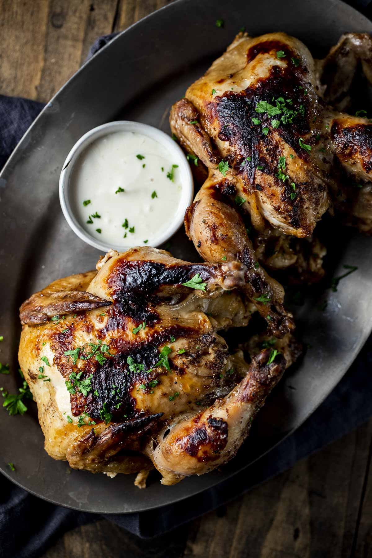 Overhead view of two Cornish hens on a platter with yogurt sauce on the side.