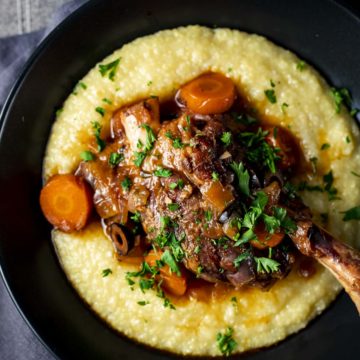 Overhead view of lamb shanks served on top of polenta in a bowl.