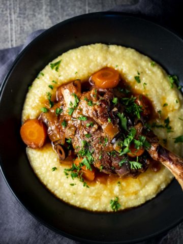 Overhead view of lamb shanks served on top of polenta in a bowl.