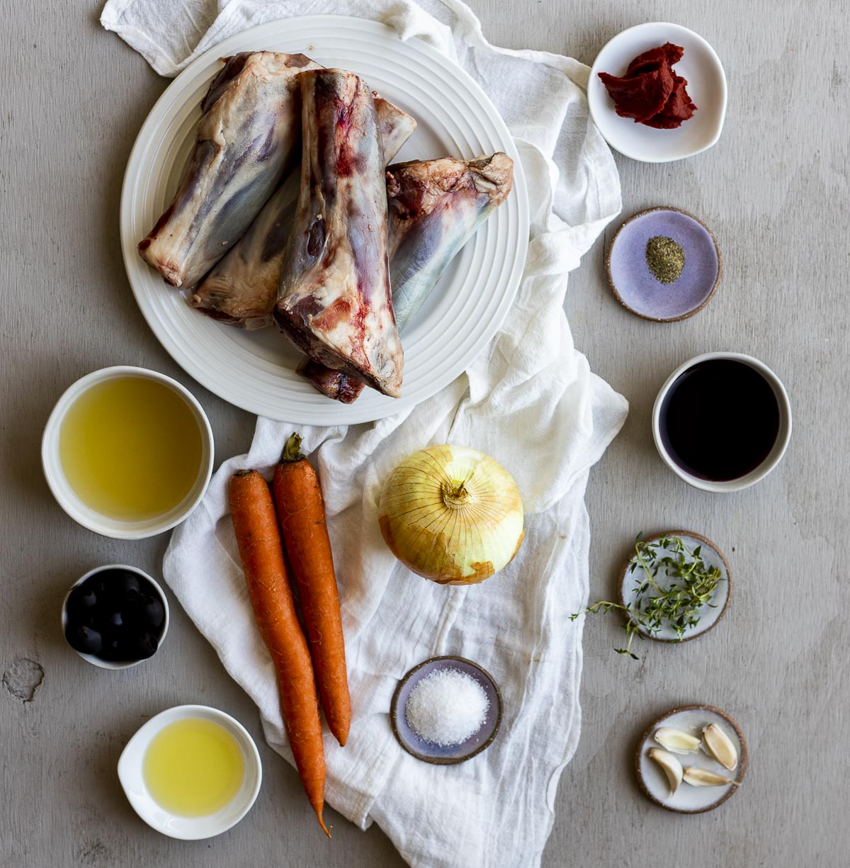 Overhead view of ingredients to make Instant Pot lamb shanks arranged individually on a white cloth.