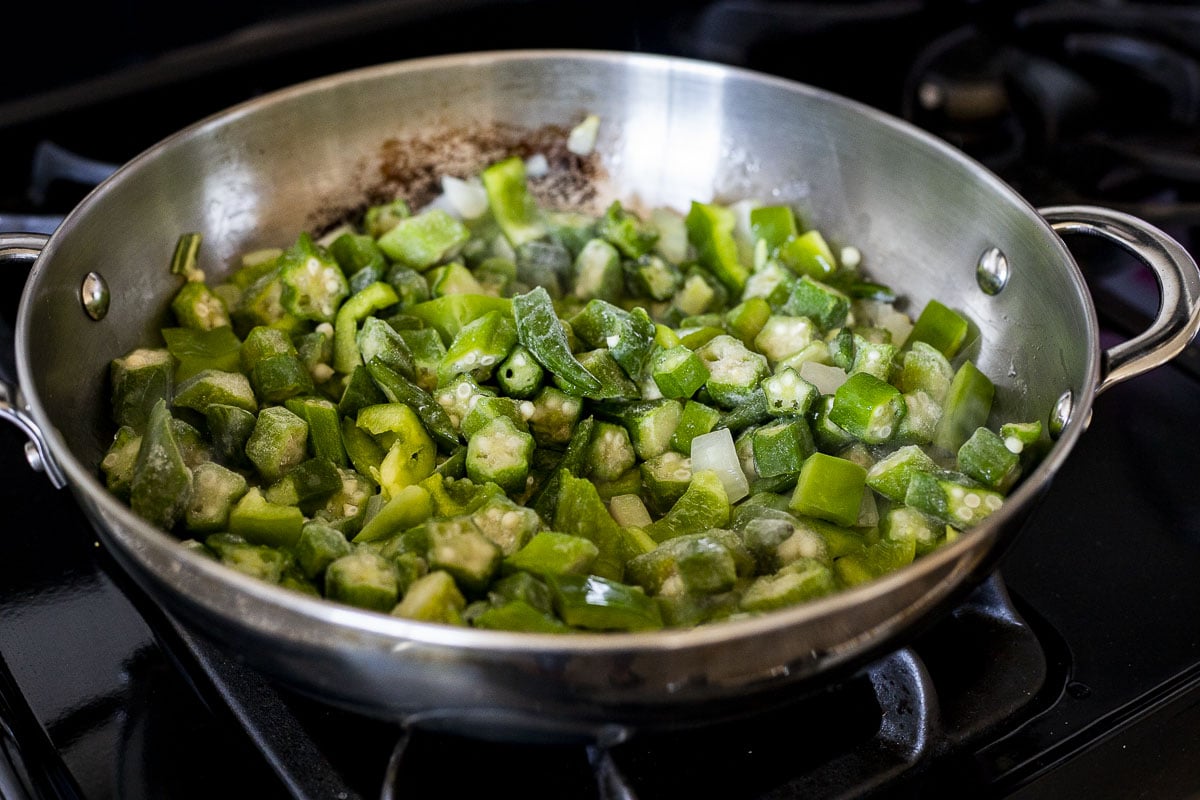 Green pepper and okra cooking in a skillet with the onions.