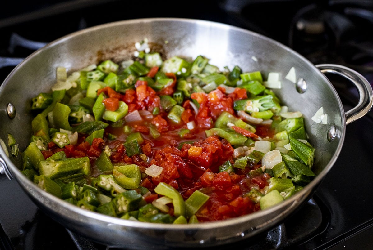 Tomatoes added to the okra mixture in a skillet.