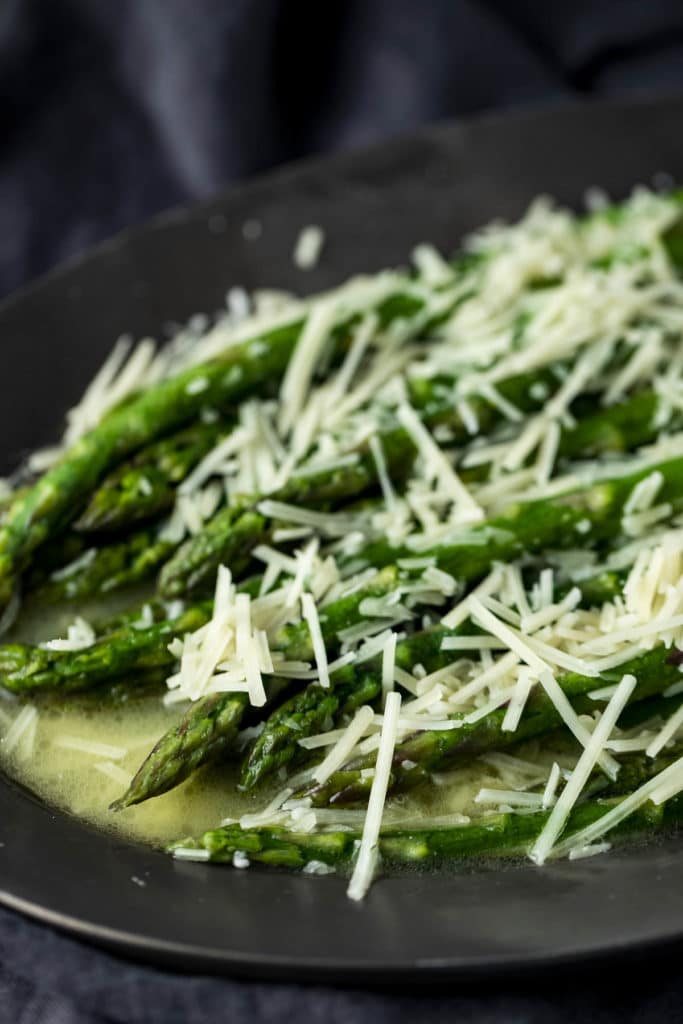 Side view of butter poached asparagus topped with grated parmesan.