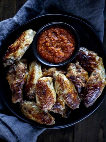 a plate of crispy chicken wings with red sauce for dipping in a bowl