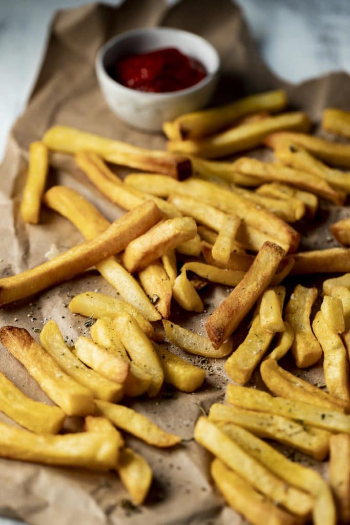 Side view of air fryer frozen french fries on brown paper with a small bowl of ketchup.