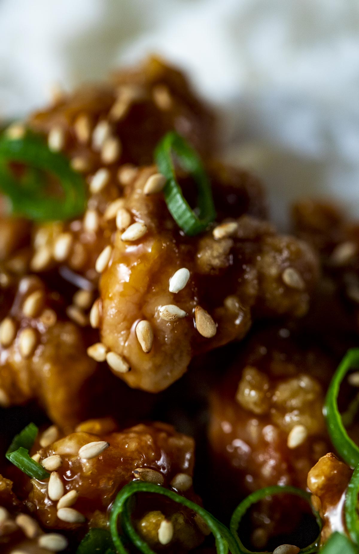 Close up of orange chicken topped with sesame seeds and green onion.