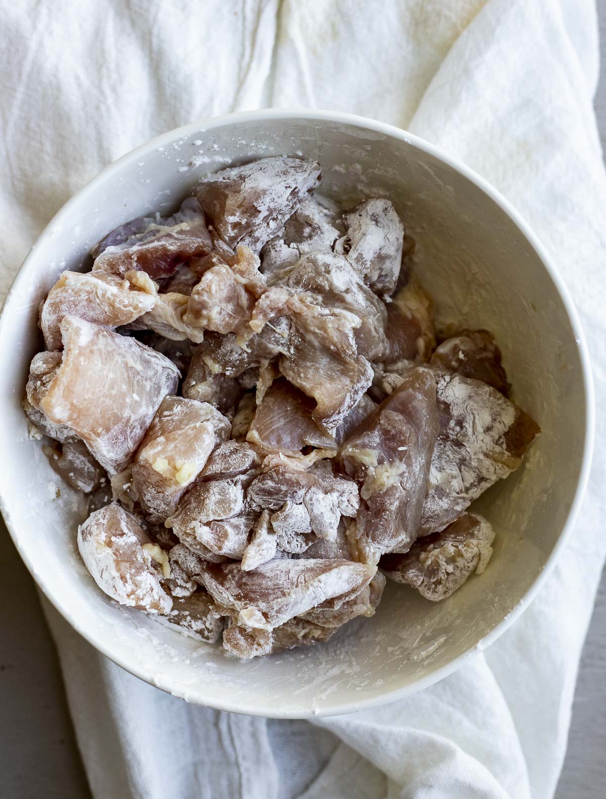 Chicken pieces coated in cornstarch in a white bowl.