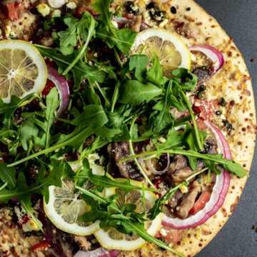 Overhead view of sardine pizza garnished with arugula and lemon slices.