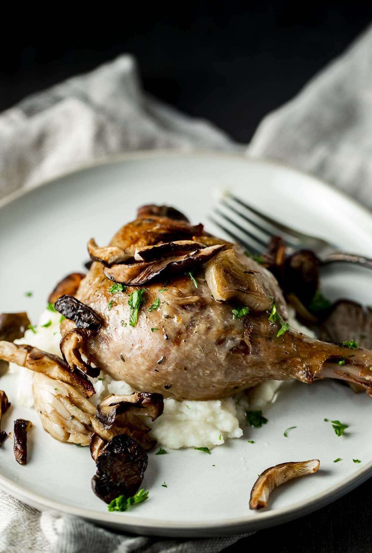 Duck leg served with mushrooms over mashed potatoes.