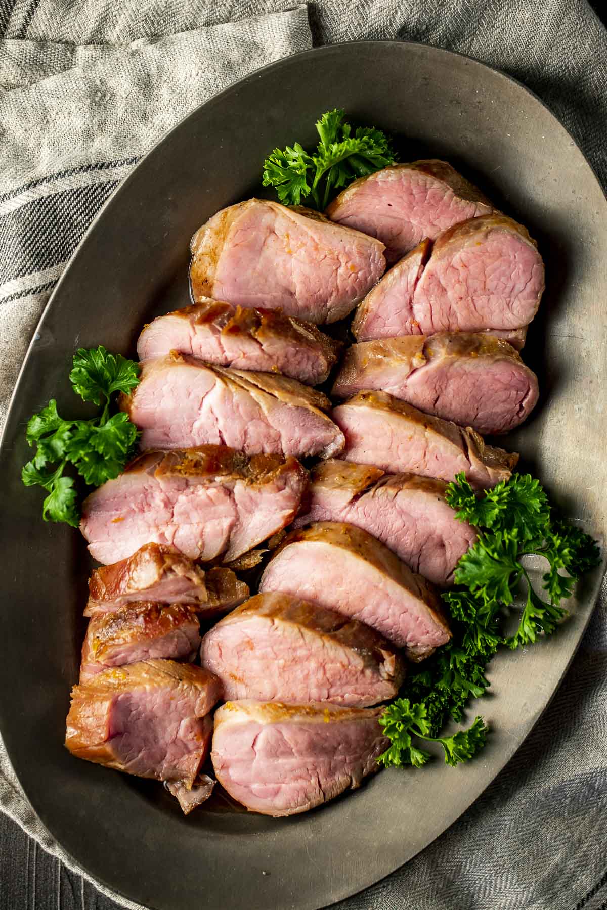 Pork tenderloin slices arranged on a platter with a herb garnish.