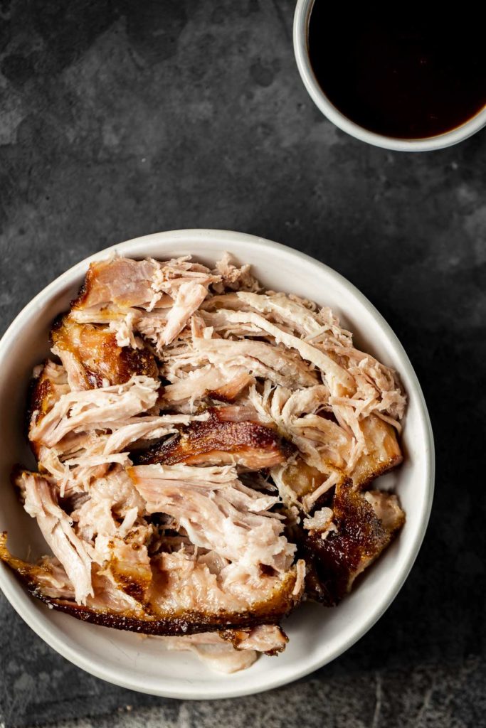 Overhead view of pulled pork in a white bowl.