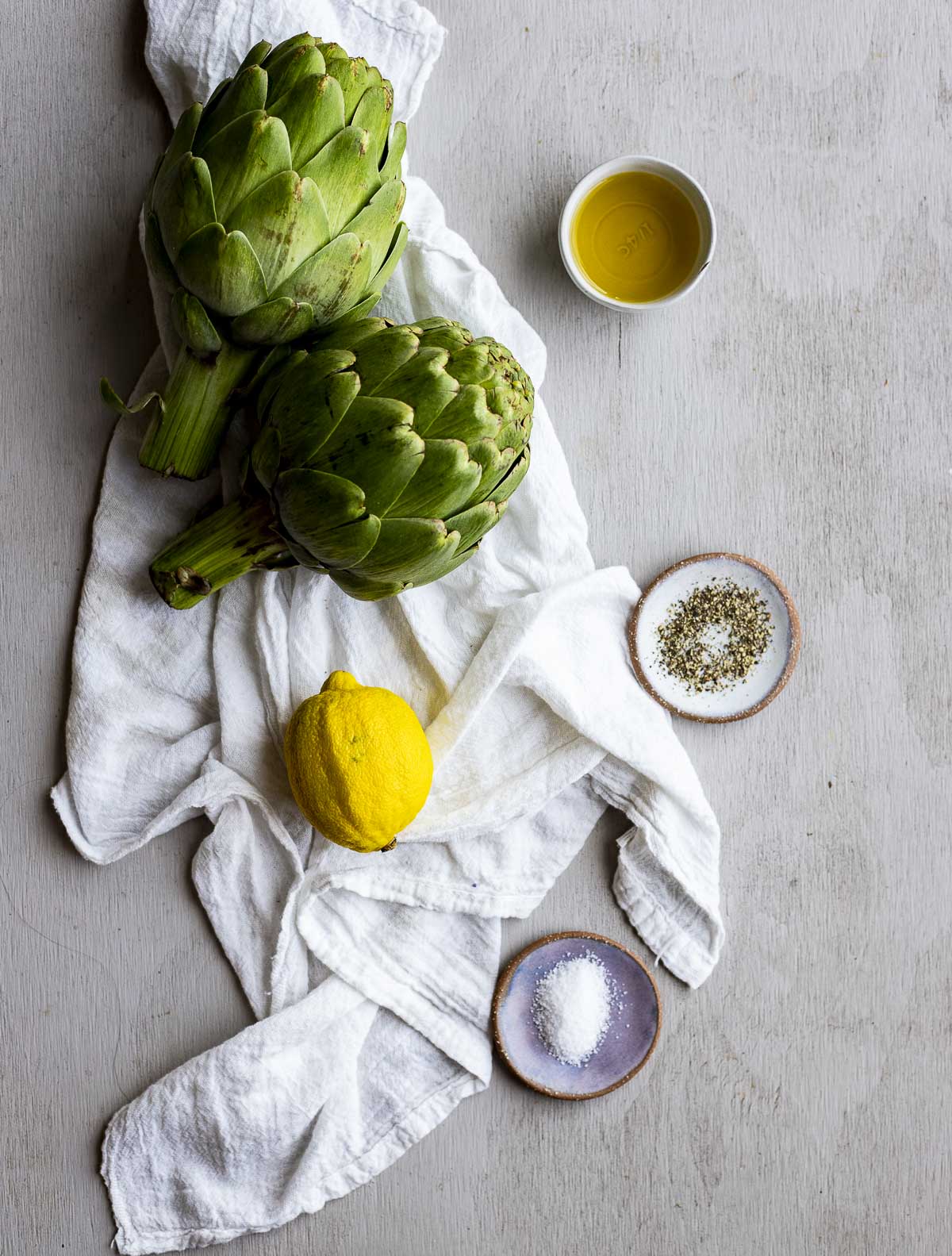 Ingredients to make air fryer artichokes arranged individually on a white cloth.