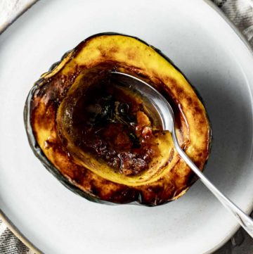 Overhead view of an air fried acorn squash half on a white plate with a spoon inserted into it.