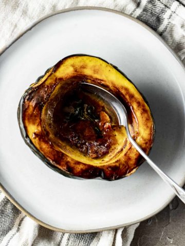 Overhead view of an air fried acorn squash half on a white plate with a spoon inserted into it.