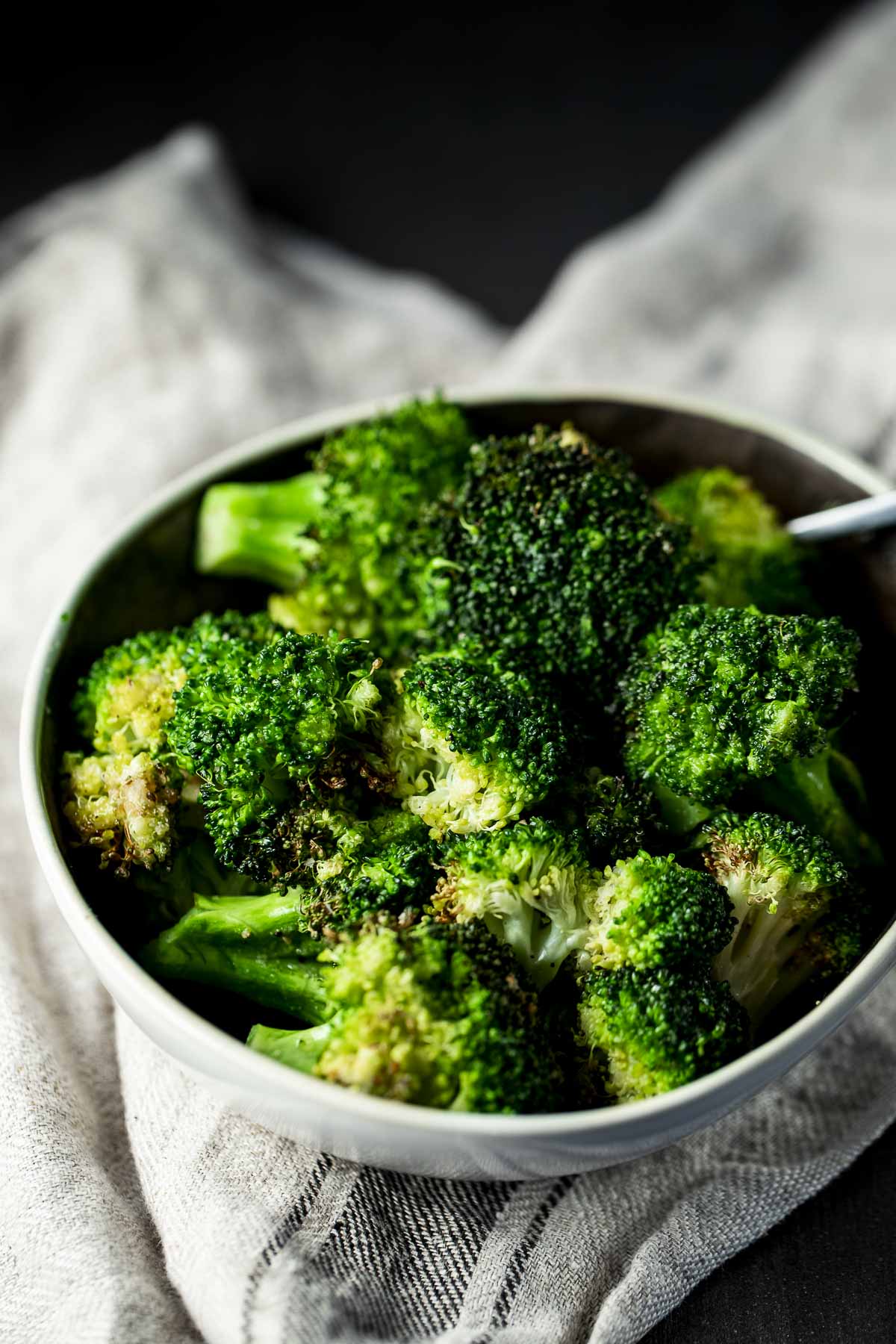 Side view of air fryer broccoli in a bowl on a cloth.
