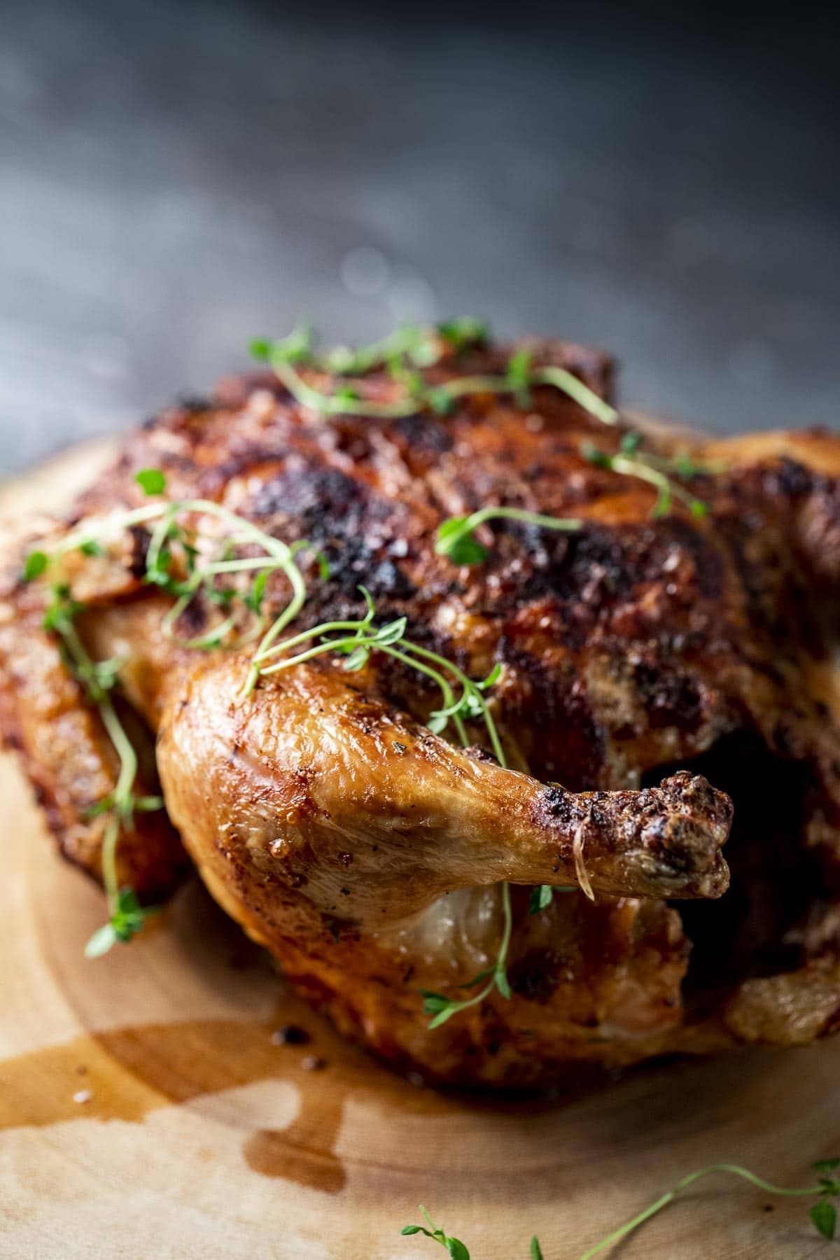 Side view of a cooked chicken on a wooden board.