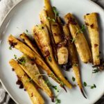 Overhead of honey roasted parsnips arranged on a plate and topped with fresh thyme.