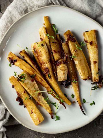 Overhead of honey roasted parsnips arranged on a plate and topped with fresh thyme.
