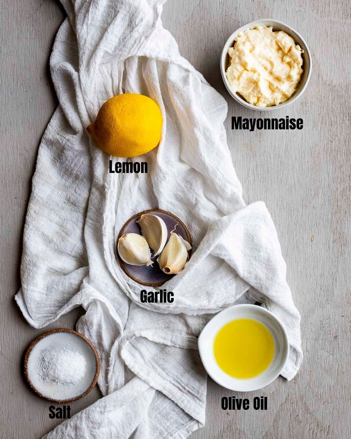 Ingredients to make garlic aioli arranged individually on a white cloth.