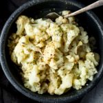 Overhead of cooked cauliflower florets in a bowl with a serving utensil.