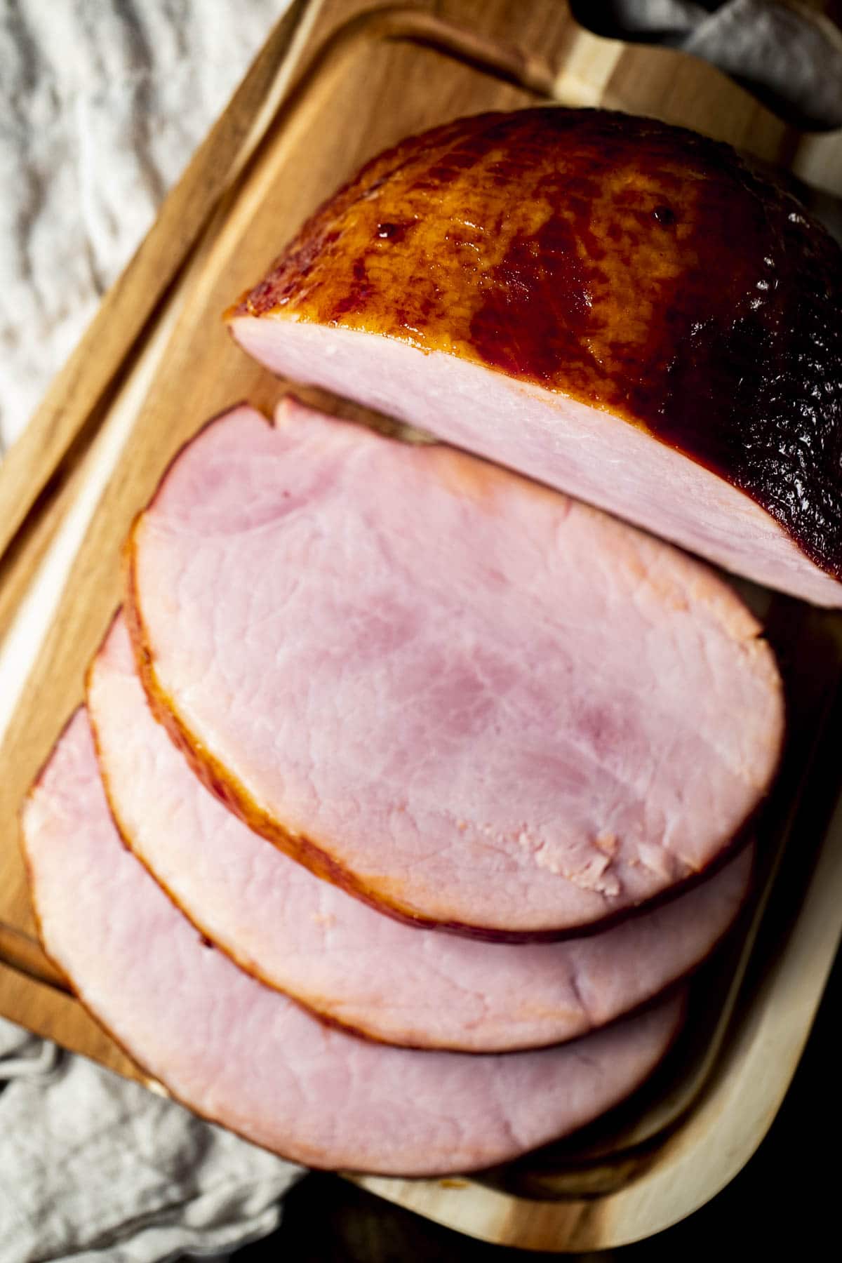 Overhead view of sliced ham on a wooden cutting board.