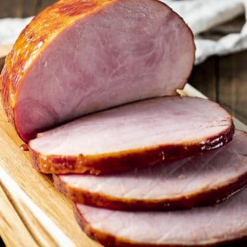 Side view of a boneless ham on a wooden board and cut into slices.